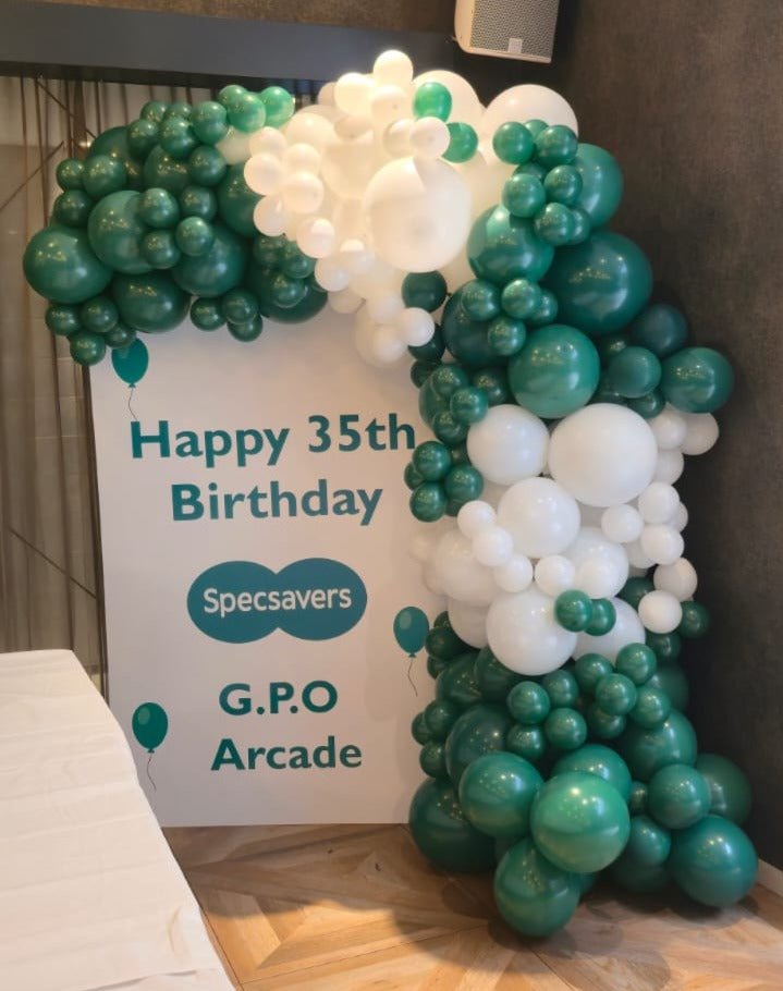 Organic Demi Arch: Latex balloon in blocked in Green and white in various sizes, Balloons going around a air board sign promoting an event. 