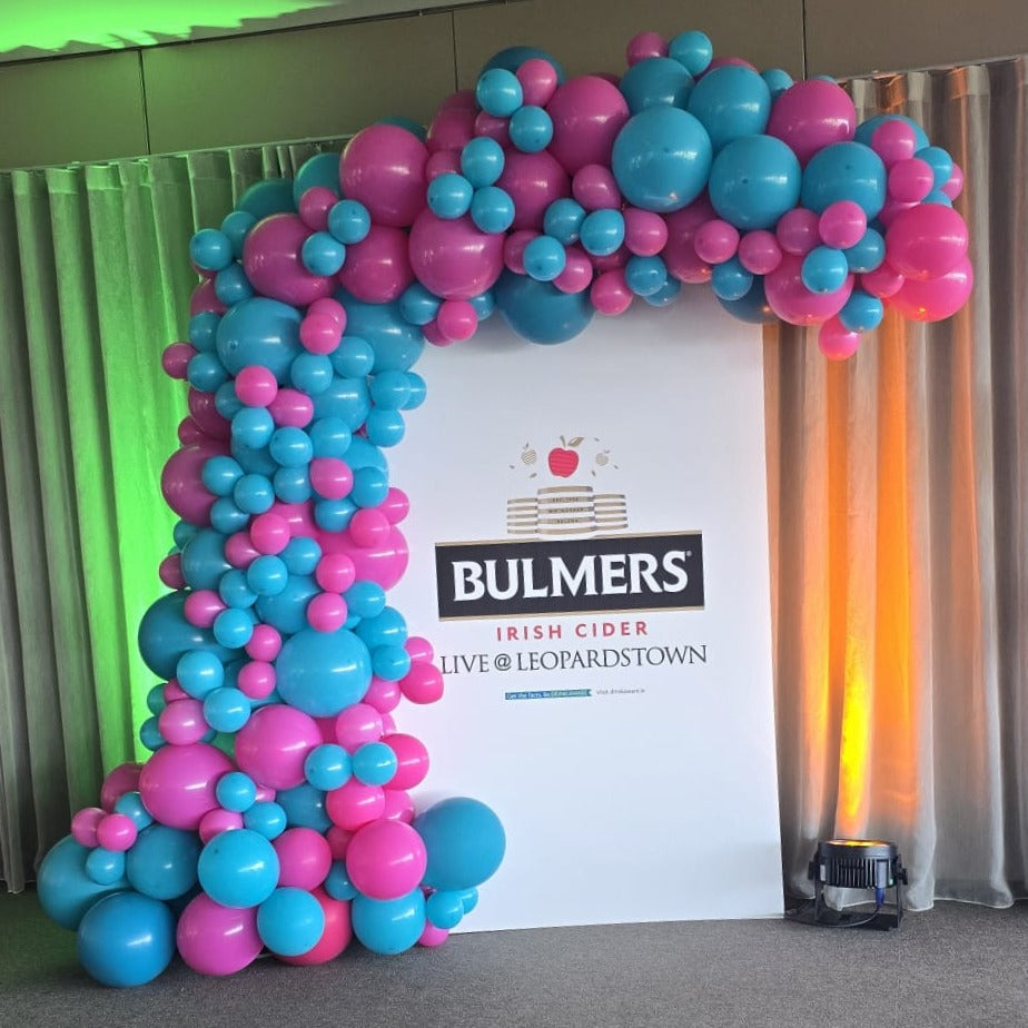 Organic Demi Arch: Latex balloon in blocked in Blue and Pink in various sizes, Balloons going around a air board sign promoting an event. 